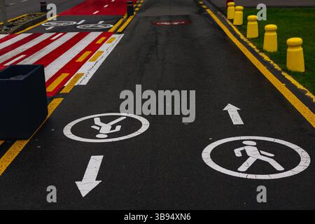 Ein ausgewiesener Fußgänger- und Fahrradweg ist mit Schildern und Linien für die Sicherheit auf der Straße gekennzeichnet. Die Markierungen und Richtungszeichen auf dem Asphalt. Stockfoto