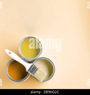 Dosen mit Farbe in Gelbtönen und Pinsel auf beigem Hintergrund, Draufsicht. Leerzeichen für Text Stockfoto