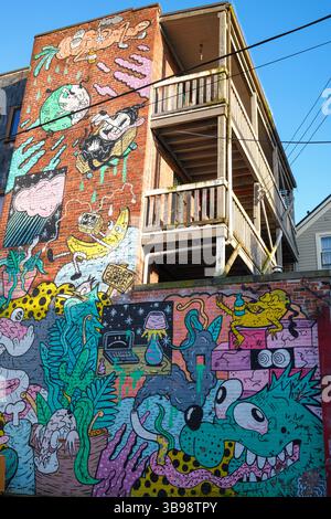 Ein Wandgemälde am Fuße einer alten Backsteinwohnung in einer Main Street Gasse in Mount Pleasant, Vancouver, BC. Stockfoto
