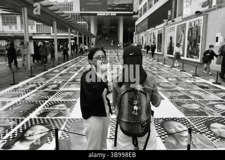 27. April 2023, HONGKONG, CHINA: In Hongkong gab es eine touristische Frau, die vor der öffentlichen Ausstellung der Werke des französischen Künstlers JR Eiscreme trinkte, 450 lächelnde Gesichter von Hongkong, die auf monochromen Drucken zum Ausdruck kamen. Im Rahmen des globalen JR-Projekts wird [ Inside Out : Harbour and the City ] derzeit in Hongkong ausgestellt.April-27.2023Hong Kong.ZUMA/Liau Chung-ren (Bild: © Liau Chung-ren/ZUMA Press Wire) Stockfoto