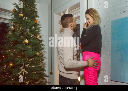 Ein verliebtes Paar steht vor dem Hintergrund eines Weihnachtsbaums, Umarmungen, Wärme einer Beziehung Stockfoto