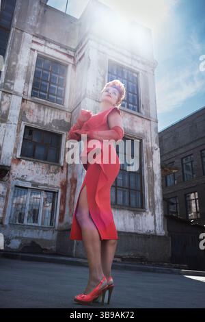 Eine rothaarige, lockige, schöne Frau in einem roten Kleid mit Volants steht auf der Straße Stockfoto