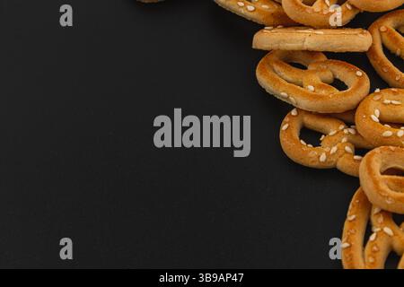 Herzhafte Brezeln in goldbraunem Farbton und Sesamsamen sind lässig auf einer schwarzen Oberfläche verteilt und eignen sich perfekt als Snack oder Party Stockfoto