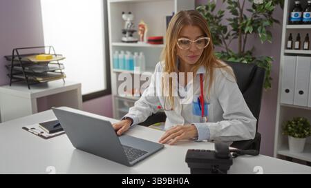 Frau Ärztin, die am Kliniktisch mit Laptop und medizinischen Geräten arbeitet und ein professionelles Gesundheitsumfeld mit Fokus auf moderne Technik präsentiert Stockfoto
