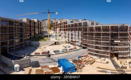 Panoramablick auf eine moderne Wohnbaustelle mit Gerüsten, Kränen und unfertigen Gebäuden unter klarem blauen Himmel in einer Stadt Stockfoto