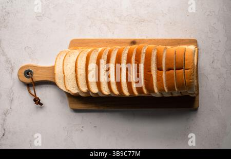 Brotlaib mit geschnittenem Weißbrot von oben auf Schneidebrett auf Steintheke. Stockfoto