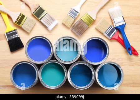 Dosen mit Farbe in Blautönen und Pinsel auf hölzernem Hintergrund, Draufsicht Stockfoto