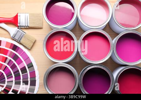 Dosen mit Farbe in Rosa, Farbpalette und Pinsel auf hölzernem Hintergrund, Draufsicht Stockfoto
