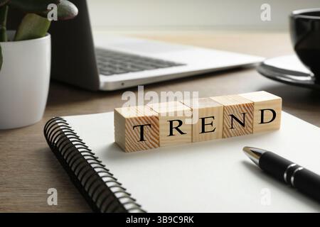 Word Trend aus Holzwürfeln auf Notizbuch. Arbeitsplatz mit Schreibwaren und Laptop auf dem Tisch Stockfoto