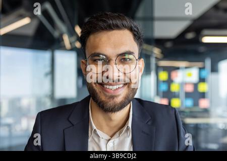 Porträt erfolgreicher junger Geschäftsmann am Arbeitsplatz im Büro. Mann, der aus nächster Nähe lächelt und in die Kamera schaut, zufriedener Investor. Stockfoto