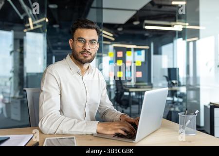 Porträt eines Reifen und seriösen Geschäftsmannes am Arbeitsplatz. Mann im Hemd, der in die Kamera schaut, mit dem Laptop im Büro arbeitet. Stockfoto