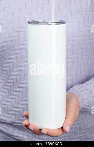 Weibliche Hände halten einen 20-oz-dünnen Becher für Sublimation. Reisebecher Strohabdeckungen Becher mit Deckel. Pullover in Flieder Stockfoto