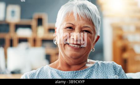 Senior, Frau und Lächeln mit Porträt zu Hause für Entspannung, Komfort und Ruhe im Ruhestand. Ältere Person, glücklich und selbstbewusst auf dem Sofa Stockfoto