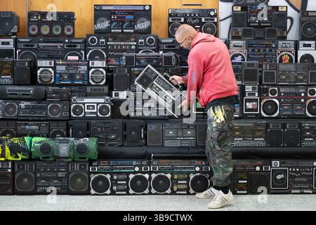Dresden, Deutschland. Mai 2025. Sebastian Girbig durchsucht seine Sammlung von rund 60 tragbaren Musiksystemen, umgangssprachlich auch Boomboxen genannt, in der ehemaligen Robotron-Kantine. Die Sammlung ist Teil des erstmals stattfindenden Hip-Hop-Festivals ALL4/1, das bis zum 11. Mai 2025 die facettenreiche Hip-Hop-Kultur in Dresden präsentieren soll. Quelle: Sebastian Kahnert/dpa/Alamy Live News Stockfoto