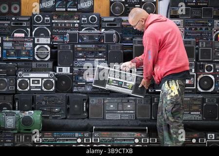 Dresden, Deutschland. Mai 2025. Sebastian Girbig durchsucht seine Sammlung von rund 60 tragbaren Musiksystemen, umgangssprachlich auch Boomboxen genannt, in der ehemaligen Robotron-Kantine. Die Sammlung ist Teil des erstmals stattfindenden Hip-Hop-Festivals ALL4/1, das bis zum 11. Mai 2025 die facettenreiche Hip-Hop-Kultur in Dresden präsentieren soll. Quelle: Sebastian Kahnert/dpa/Alamy Live News Stockfoto