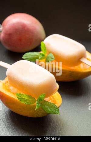 Mangoeis wird elegant in frischen Mangohälften serviert, garniert mit Minzblättern. Die leuchtenden Farben strahlen unter hellem Sonnenlicht und sorgen für ein erfrischendes Desserterlebnis. Stockfoto
