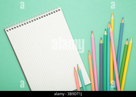 Offenes Notizbuch mit buntem Bleistift auf mintfarbenem Hintergrund. Draufsicht Stockfoto