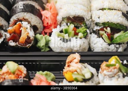 Frische Sushi-Brötchen aus der Nähe. Japanische Küche zum Mitnehmen. Leckerer Reis mit Fisch und Gemüse. Wasabi und Ingwer serviert. Asiatisches Mittagessen in Plastikkiste. Stockfoto