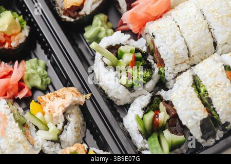 Verschiedene Sushi-Rollen in schwarzem Tablett. Japanische Meeresfrüchte mit Reis, Gemüse und Wasabi. Frisches Essen zum Mitnehmen. Gesundes traditionelles asiatisches Mittagessen Hintergrund. Stockfoto