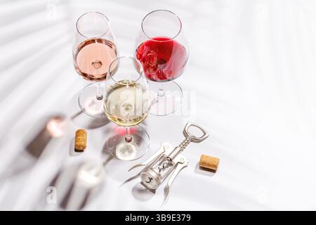Drei Weingläser gefüllt mit Rot-, weiß- und Rosenwein, anmutig auf einem hellen, minimalistischen Hintergrund. Eine lebendige Darstellung der Vielfalt der Weine Stockfoto