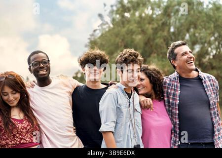 Fröhliche multiethnische Teenager und Erwachsene umarmen sich und lachen draußen an einem hellen Tag, symbolisieren Inklusion, Freundschaft und Glück. Stockfoto