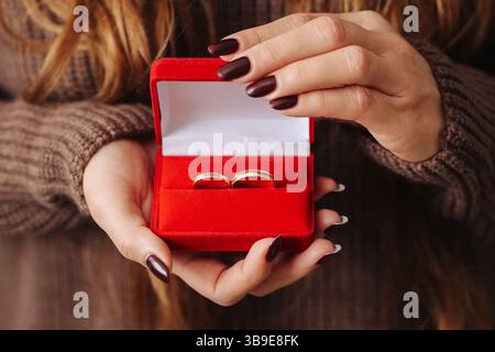 Rote Ringbox mit goldenen Eheringen. Frau mit romantischem Verlobungsgeschenk. Vorschlag und Eheschließungskonzept. Hintergrund des Liebesymbols. Stockfoto