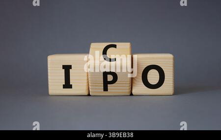 ICO vs. IPO-Symbol. Gedrehte Holzwürfel mit den Worten IPO und ICO. Schöner grauer Hintergrund. ICO vs IPO und Geschäftskonzept. Kopierbereich Stockfoto