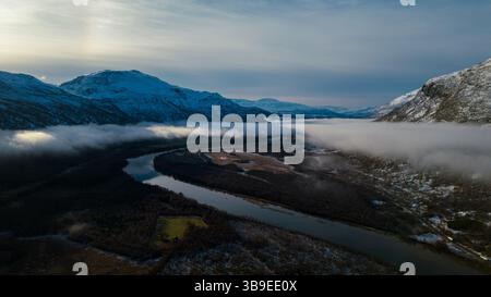 Wunderschöne Flußkulisse in Nordnorwegen, bedeckt mit Wolken und Nebel, umgeben von Bergen. Winding River wurde auf eine Drohne geschossen. Stockfoto
