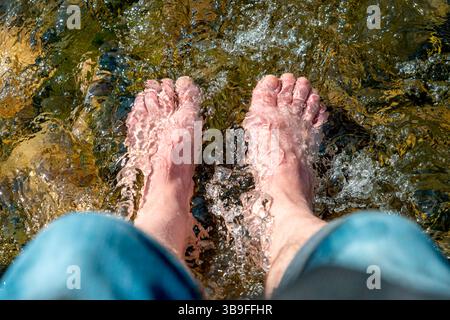 Fließendes Wasser zwischen Steinen wäscht um die Füße eines Mannes Stockfoto