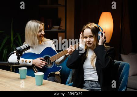 Zwei Musikerinnen spielen und nehmen in einem Heimstudio einen Song mit Akustikgitarre und professionellem Mikrofon auf Stockfoto