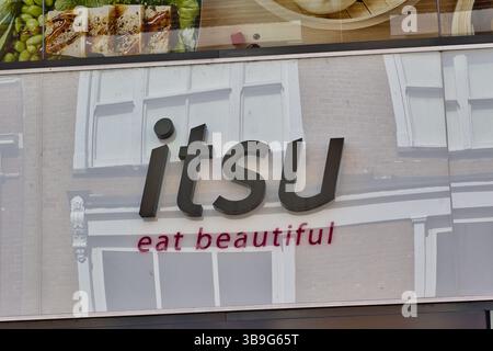 Nahaufnahme des „itsu“-Restaurantschilds. Die Buchstaben sind dunkel und fett, mit „Eat Beautiful“ unten in einem helleren Rot. Die Gebäudereflexion ist brillant Stockfoto