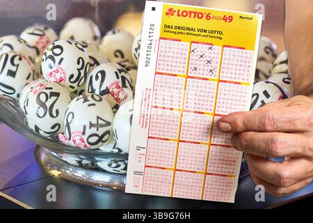 Bayern, Deutschland - 9. Mai 2025: FOTOMONTAGE, Ein abgeschlossenes Lotterieticket wird neben einer Schüssel voller Draw Balls abgehalten - der Moment vor der Lotterieverlosung, der Hoffnung auf Glück und großen Sieg weckt. *** FOTOMONTAGE, ein ausgefüllter Lottoschein wird neben einer Schale voller Ziehungsbälle halten der Moment vor der Lottoziehung, der Hoffnung auf Glück und einen großen Gewinn weckt. Stockfoto