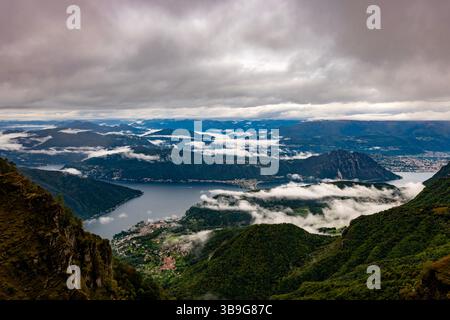 Wunderschöner Blick über die Stadt und den Luganer See und die Schweizer Alpen mit Wolken an einem bewölkten Tag im Herbst in Lugano, Tessin, Schweiz. Stockfoto
