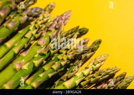 Nahaufnahme frischer grüner Spargelspeere auf einem leuchtend gelben Hintergrund, die ihre natürlichen Strukturen und Farben hervorheben. Perfekt für gesundes Essen Stockfoto