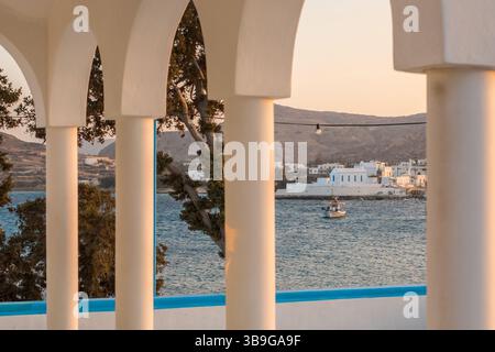 Dieses malerische Bild zeigt Pollonia, ein bezauberndes Küstendorf auf der Insel Milos, Griechenland, eingerahmt von einem weißen gewölbten Balkon bei einem ruhigen Sonnenuntergang. Stockfoto