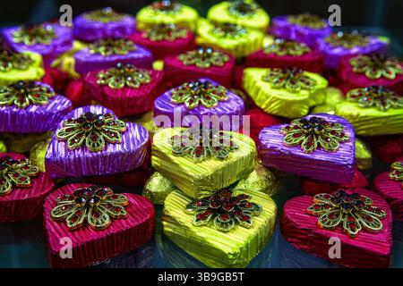 Bunte Schokoladenbonbons in Herzform in glänzender Verpackung mit Geschenkbrosche, Blick von oben. Stockfoto