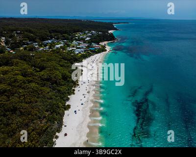 Blick aus der Vogelperspektive auf einen ruhigen Strand mit türkisfarbenem Wasser und üppigem Wald rund um eine kleine Küstenstadt in Jervis Bay, Australien. Die Sandküste i Stockfoto