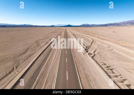 Eine gerade Straße führt durch eine weite Wüstenlandschaft der argentinischen Puna und führt in ferne Berge unter einem klaren blauen Himmel, die einen Sinn wecken Stockfoto