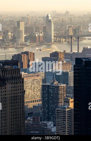 Blick von oben auf New York City bei Sonnenuntergang und das goldene Licht über die Gebäude, den Fluss und die Brücken. Atemberaubende urbane Landschaft mit einem warmen Grau Stockfoto