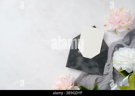 Elegantes Hochzeitspapier mit einem eleganten Umschlag mit einer leeren Einladung umgeben von zarten weißen Blumen auf einer weichen Marmoroberfläche, ideal für Stockfoto