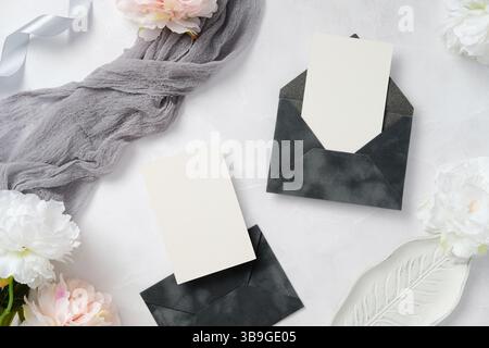 Ein elegantes Layout für Hochzeitspapiere mit eleganten dunklen Umschlägen, leeren Karten, zarten Blumen und weichem Stoff, perfekt für Einladungen oder Stockfoto