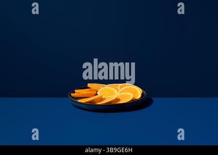 Auf einem Teller angeordnete Scheiben frischer Orangen vor einem kräftigen blauen Hintergrund. Die lebendigen Farben erzeugen einen auffälligen Kontrast und heben die Frucht hervor Stockfoto