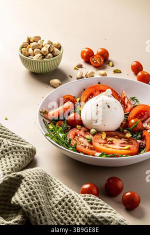 Ein lebendiger Salat mit cremigen Burrata, saftigen Tomaten und knusprigen Pistazien. Serviert in einer weißen Schüssel mit frischer Textur, perfekt für eine Nährstoffzufuhr Stockfoto