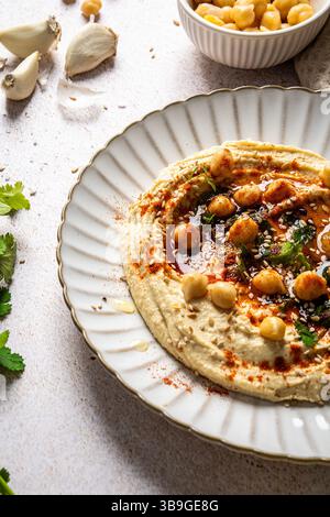 Cremiger Hummus serviert auf einem weißen Teller, garniert mit ganzen Kichererbsen, Paprika, Olivenöl und frischen Kräutern. Perfekt für Liebhaber der mediterranen Küche. Stockfoto