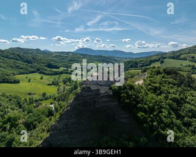 Drohnenblick auf eine historische Steinburg auf einem felsigen Hügel, umgeben von grünen Hügeln und Tälern in Marken, Italien. Ein klarer Himmel und weit weg Stockfoto