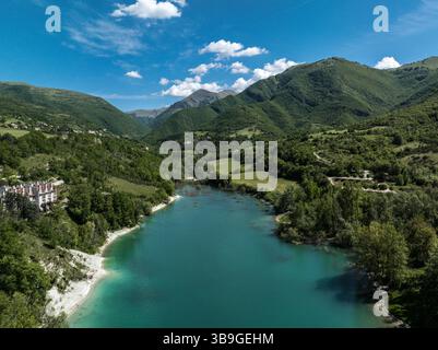 Blick aus der Vogelperspektive auf den Lago di Fiastra in Italien, mit türkisfarbenem Wasser, üppig grünen Hügeln und klarem blauen Himmel, der eine ruhige und malerische Atmosphäre schafft Stockfoto