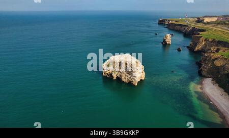 Blick aus der Vogelperspektive auf felsige Klippen und Meeresstapel entlang einer Küste. Türkisfarbenes Wasser dominiert die Szene am Marsden Beach, Großbritannien. Stockfoto