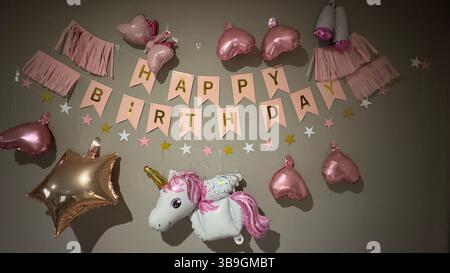 Geburtstagsdekoration mit einem „Happy Birthday“-Banner, Ballons und einer Sterngirlande auf einer grauen Wand. Stockfoto