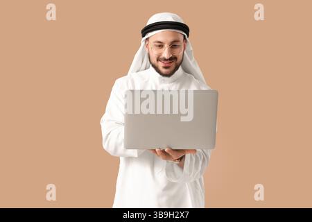 Arabischer Geschäftsmann, der mit Laptop auf beigefarbenem Hintergrund arbeitet Stockfoto