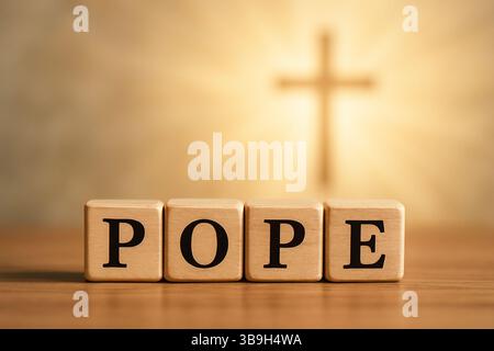 Das Wort des Papstes ist auf vier Holzblöcken geschrieben, die auf einem Tisch stehen, mit einem verschwommenen Kreuz im Hintergrund und warmer Beleuchtung Stockfoto